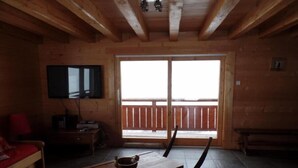 Et interiør af en træhytte med et træbord, et fjernsyn ophængt på væggen og en balkon med gelænder af træ.