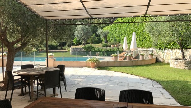 An outdoor patio with a pool, surrounded by greenery and stone walls.