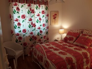 A bedroom with a floral bedspread, a bedside lamp, a chair, and a painting on the wall. - Single-storey house 110m², residential area, 500m from town center (Mirande)