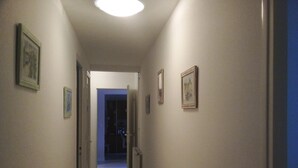 A narrow hallway with framed pictures on the walls, a door at the end, and a ceiling light. - Single-storey house 110m², residential area, 500m from town center (Mirande)