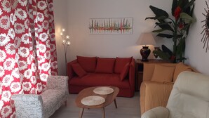 A living room with a red sofa, a beige armchair, a small coffee table, and a patterned ottoman. - Single-storey house 110m², residential area, 500m from town center (Mirande)