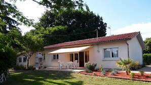 A single-story house with a red-tiled roof, a patio with white chairs, and a small garden with various plants. - Single-storey house 110m², residential area, 500m from town center (Mirande)