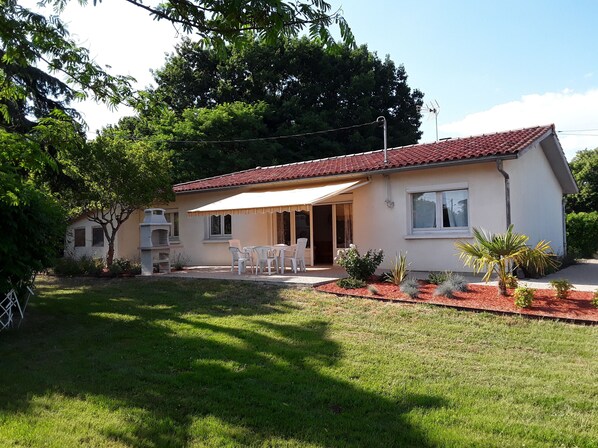 A single-story house with a red-tiled roof, a patio with white chairs, and a small garden with various plants. - Single-storey house 110m², residential area, 500m from town center (Mirande)