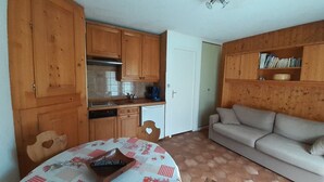 A compact living space with wooden cabinets, a kitchenette, a dining table with a checkered tablecloth, and a sofa. - East-facing studio cabin for 4 guests, pet-friendly (Valloire)