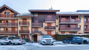 A multi-story building with balconies, a parking lot with several cars, and a snow-covered ground. - East-facing studio cabin for 4 guests, pet-friendly (Valloire)