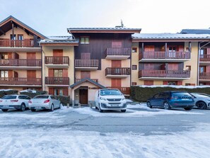 A multi-story building with balconies, a parking lot with several cars, and a snow-covered ground. - East-facing studio cabin for 4 guests, pet-friendly (Valloire)