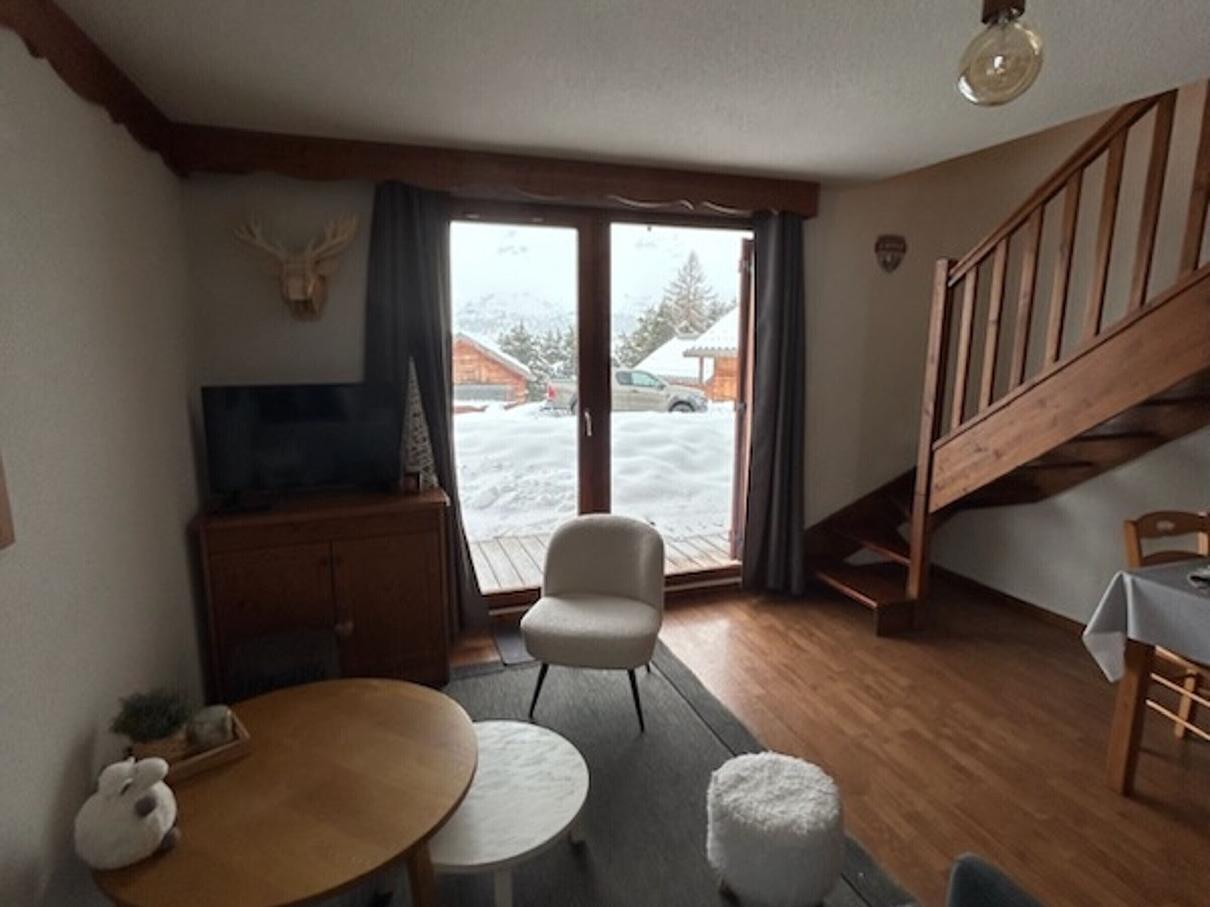Uma sala de estar aconchegante com uma escada de madeira, televisão, mesa de jantar e vista para uma área externa coberta de neve.