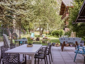 An outdoor patio with a table and chairs, surrounded by greenery and a swing set. - Spacious apartment, pets welcome - 11 guests (Valloire)