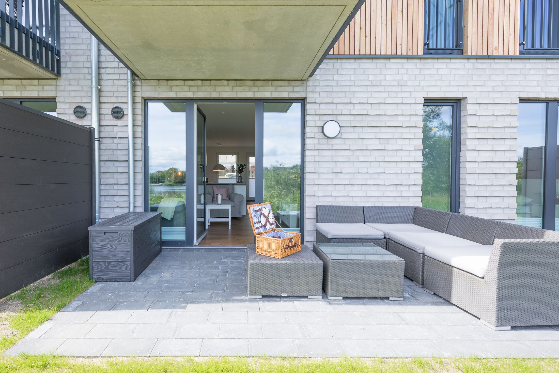 Patio esterno moderno con un divano grigio, un tavolino in vimini e un cesto in vimini.