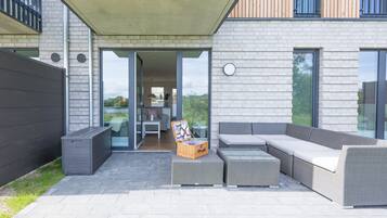 Patio esterno moderno con un divano grigio, un tavolino in vimini e un cesto in vimini.
