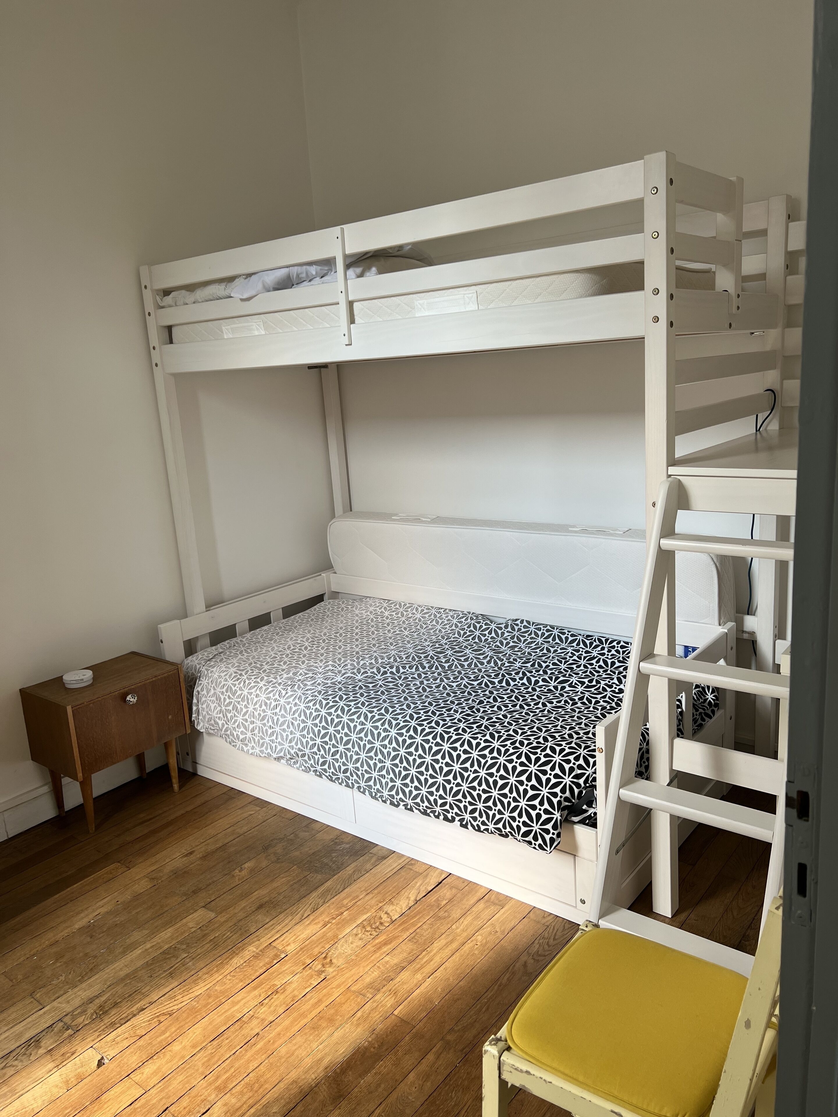 A bunk bed with a wooden nightstand and a yellow chair.