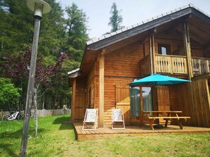 Una cabaña de madera con balcón, mesa de picnic y dos sillones.