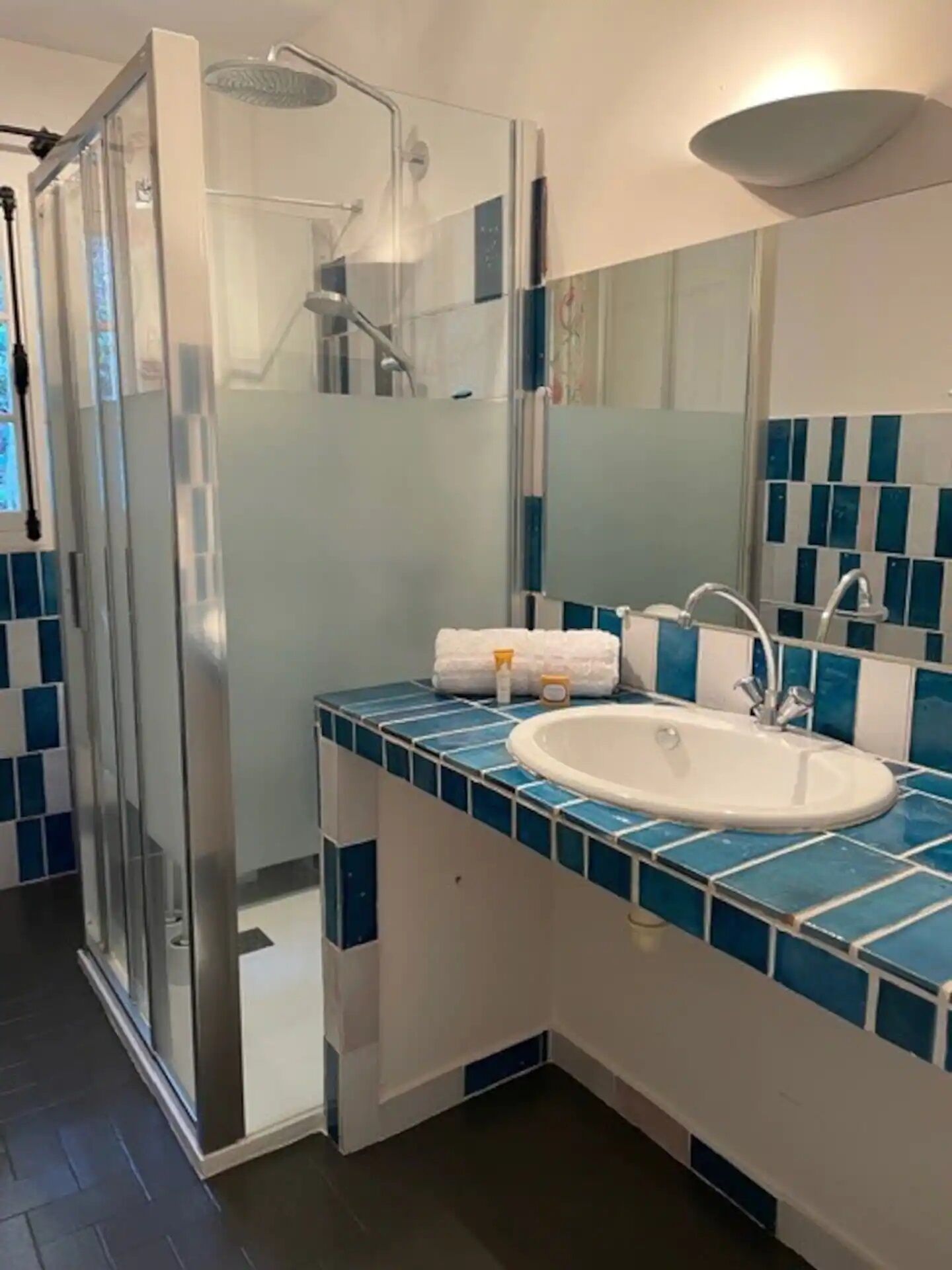 A bathroom with a glass-enclosed shower, a white sink, and blue-tiled countertops.