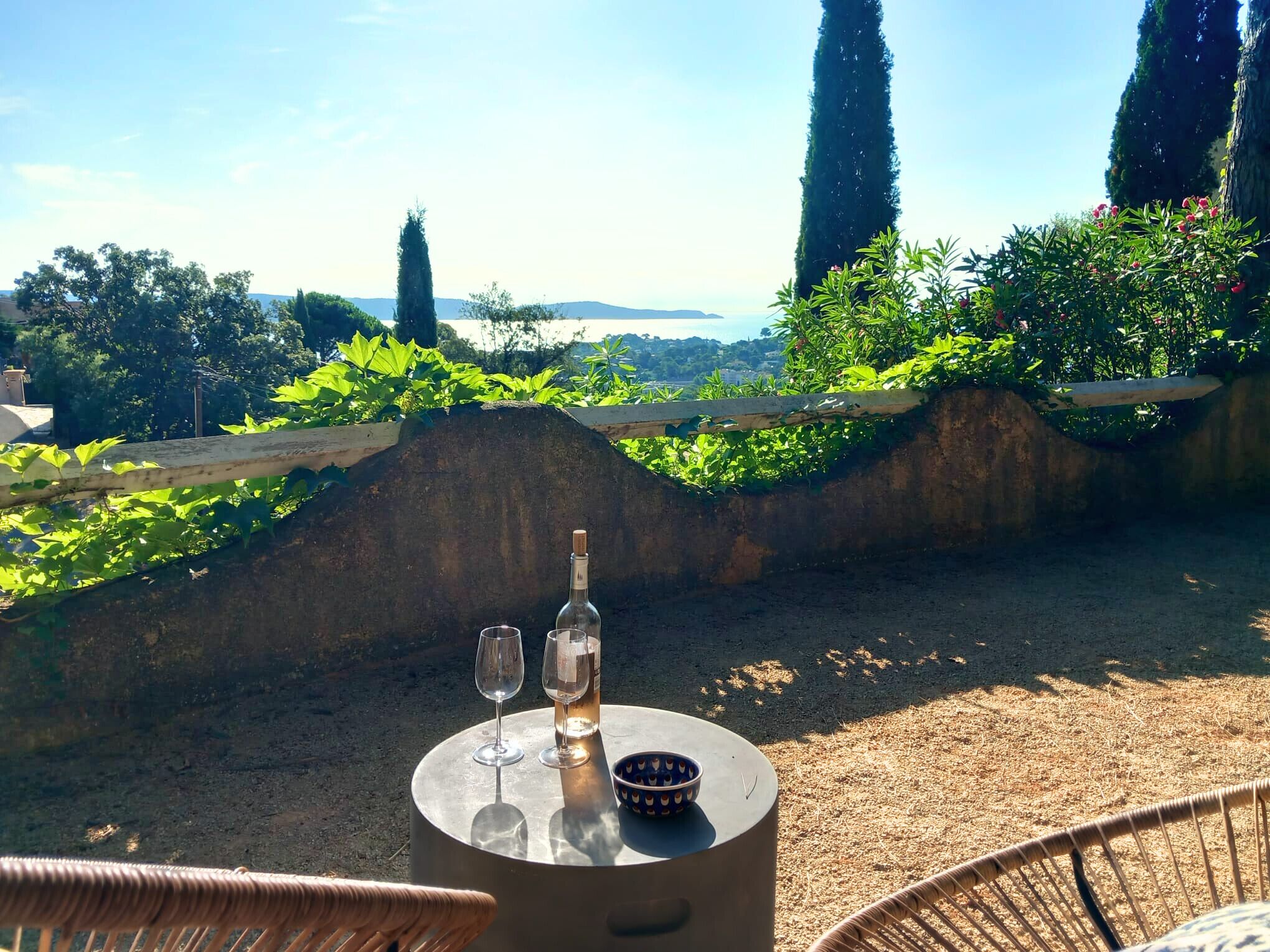 Ein Tisch mit einer Flasche und zwei Gläsern, vor einer grünen Kulisse und weiter Ferne.