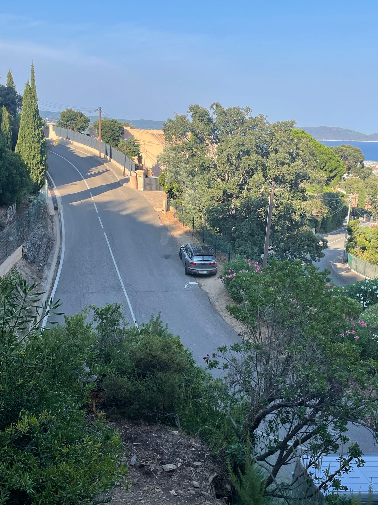 A curved road with a car parked on the side, surrounded by greenery and trees.