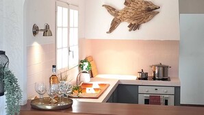 A kitchen with a wooden fish wall art, a window with blinds, a countertop with glasses and a bottle, and a stove. - Villa with heated pool and panoramic views of the Gulf of Saint Tropez (Cavalaire-sur-Mer)