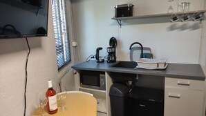 Cuina compacta amb microones, cafetera i un petit rentapel. Hi ha una ampolla de vi i un got sobre una taula, i es veu un gresol.