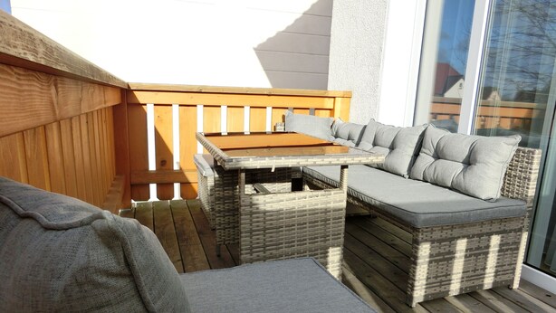 Um terraço com mobiliário de vime, incluindo uma mesa e dois sofás, e um corrimão de madeira.