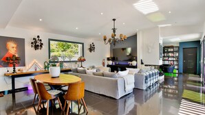 Ein modernes Wohnzimmer mit einer Couch, einem Esstisch mit Stühlen, einer Chandelüster und einem Fernseher.
