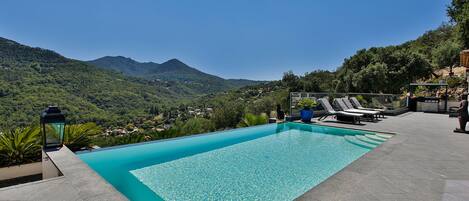 A swimming pool with a view of mountains, lounge chairs, and a stone pathway.