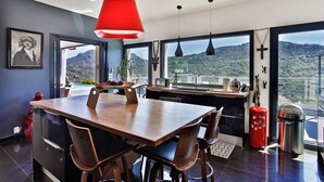 Ein moderner Essbereich mit Holztisch und -stühlen, einer roten Pendelleuchte und Blick auf eine gebirgige Landschaft durch große Fenster.