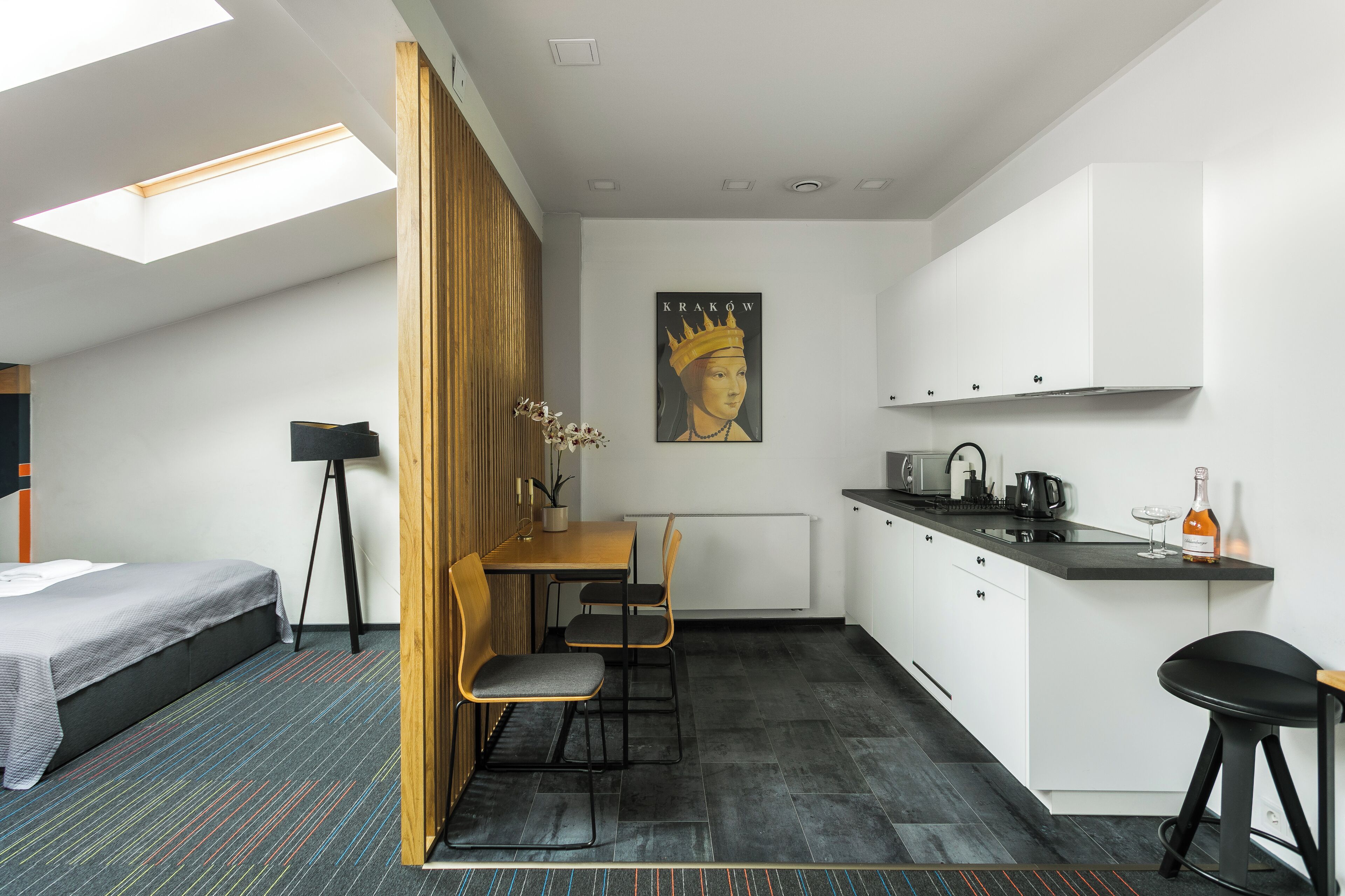 A compact room with a bed, a small dining table with chairs, a kitchenette, and a skylight.