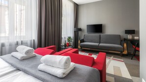 A modern hotel room with a bed, red and gray sofas, a flat-screen TV, and a large window with curtains. - Dada Premium Aparthotel (Kraków)