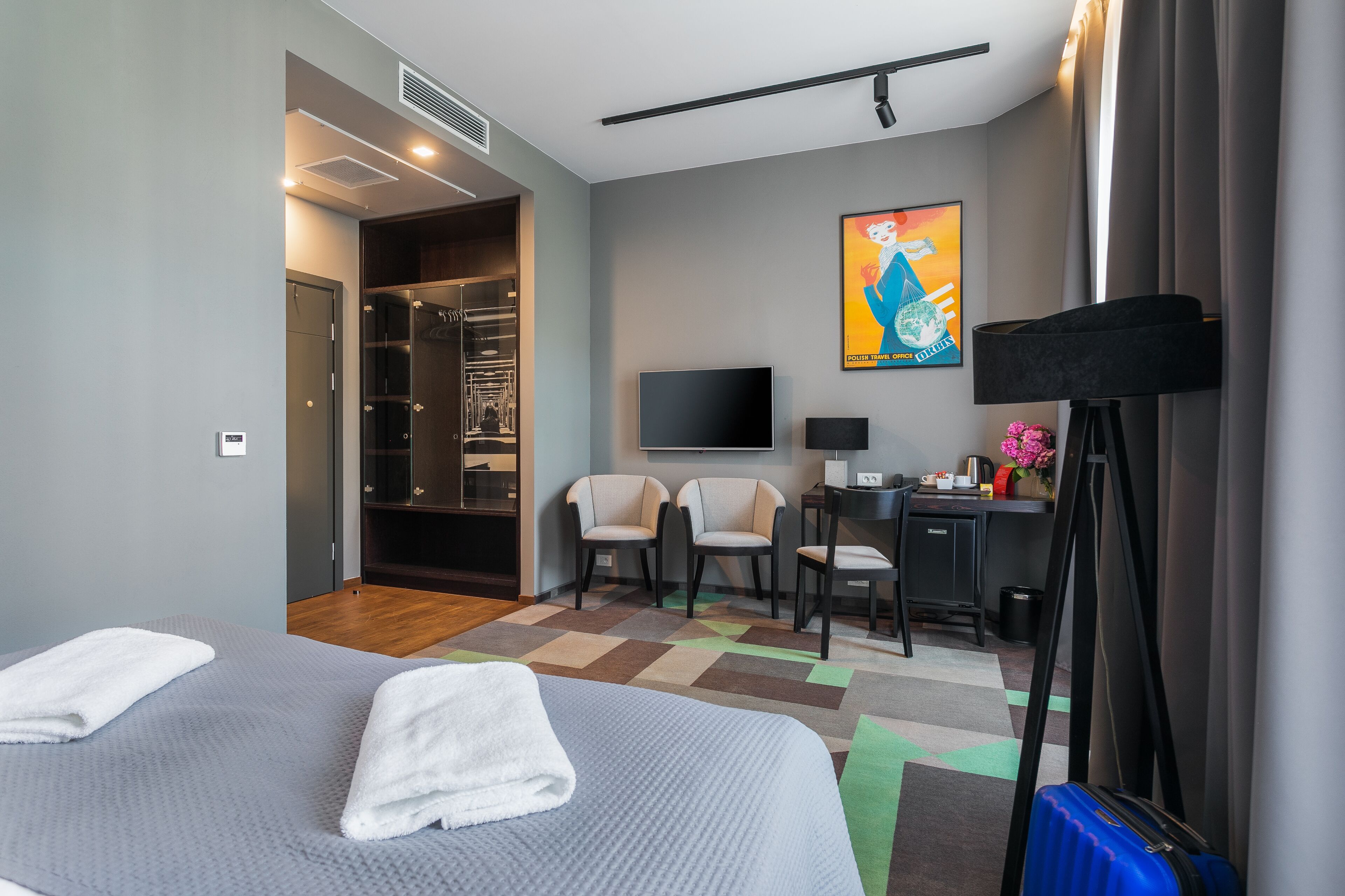Et moderne hotelværelse med seng, to stole, et skrivebord, et fjernsyn og et bruseområde.