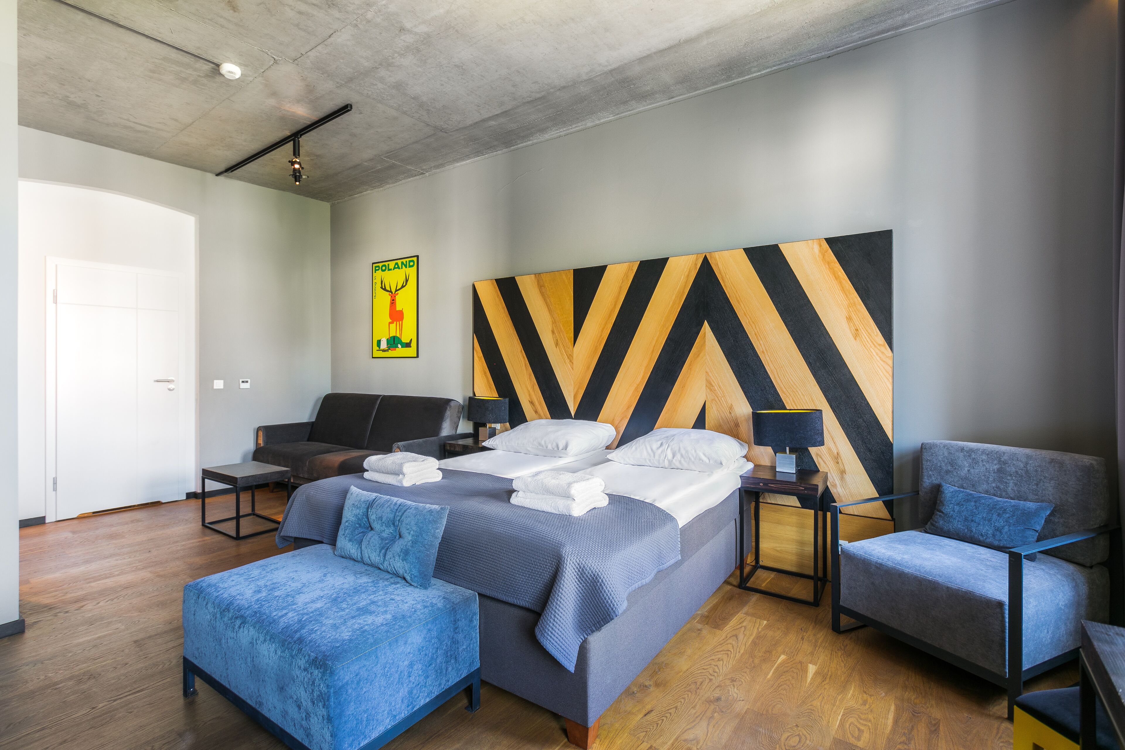 Une chambre d’hôtel moderne, dotée d’un grand lit, de deux fauteuils, d’une petite table et d’une œuvre d’art accrochée au mur.