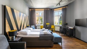 A modern hotel room with a large bed, a desk, a TV, and a view of the city. - Dada Premium Aparthotel (Kraków)