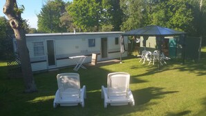 Una casa mobile con due sedie da giardino bianche davanti, un tavolo e una zona coperta con sedie.