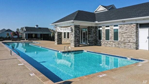 A swimming pool with a 'NOW LEASING' sign, stone building, and a clear blue sky.