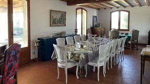 A dining area with a large table set for six, surrounded by white chairs, a blue tablecloth, and a wooden ceiling with exposed beams.