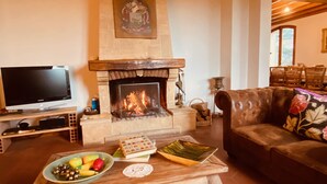A living room with a fireplace, a television, a sofa, and a table with fruits and books.