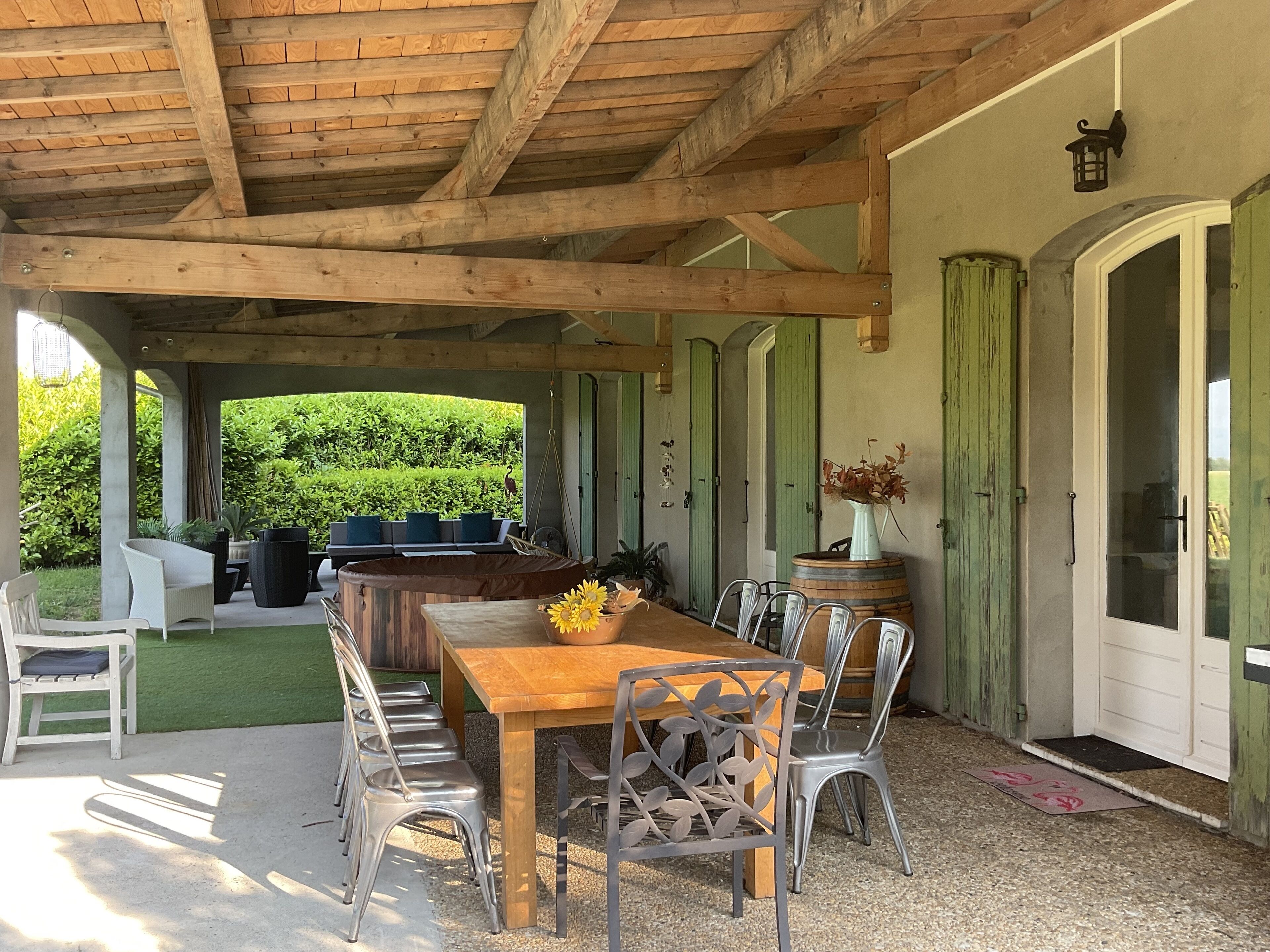 Un patio techado al aire libre con una mesa y sillas de madera, una silla colgante y vistas a un jardín verde.