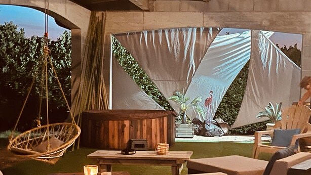 An outdoor seating area with cushioned chairs, a hanging chair, and a wooden table with a candle.