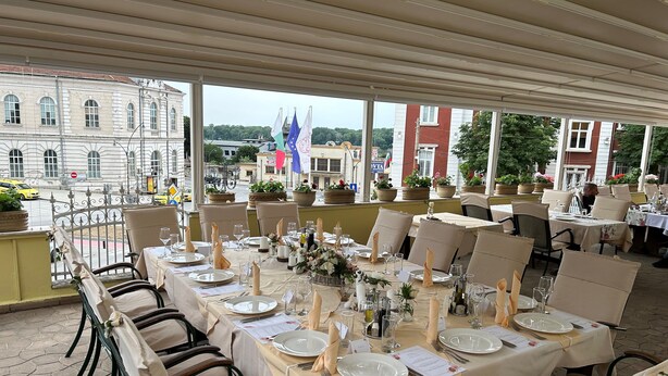 An outdoor dining area with tables set for a meal, surrounded by potted plants and overlooking a cityscape. - Anna Palace Hotel (Ruse)