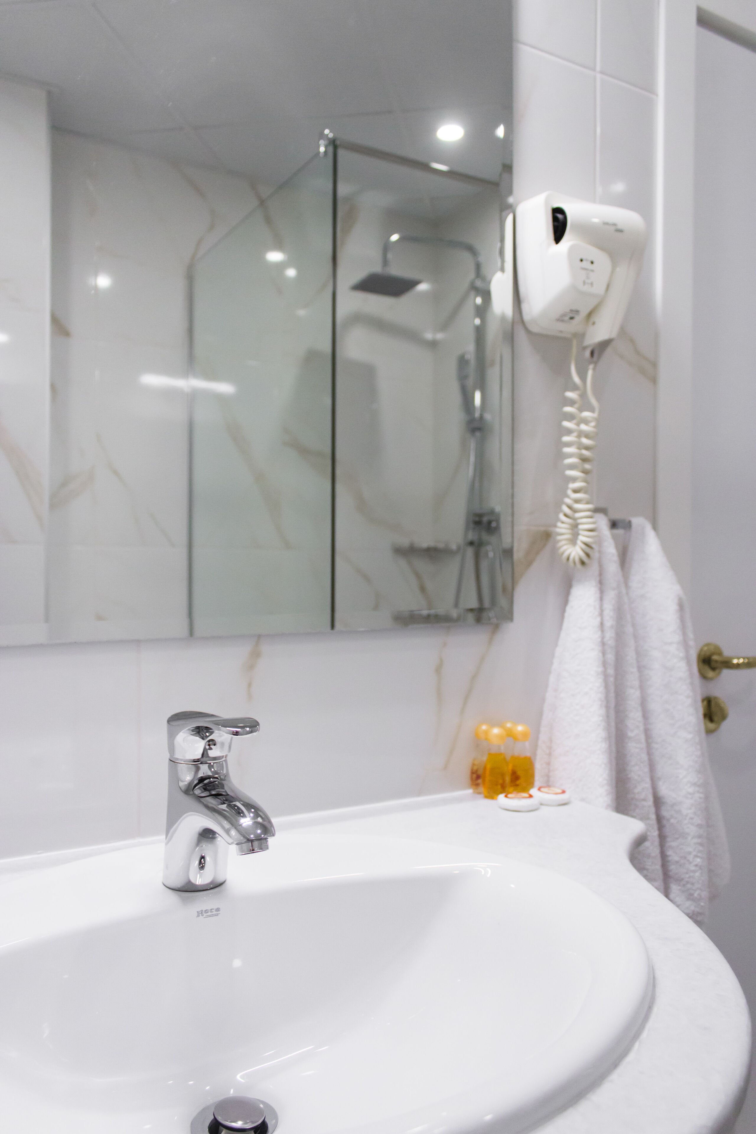 A bathroom with a white sink, a mirror, a towel hanging on the wall, and a hairdryer mounted on the wall.
