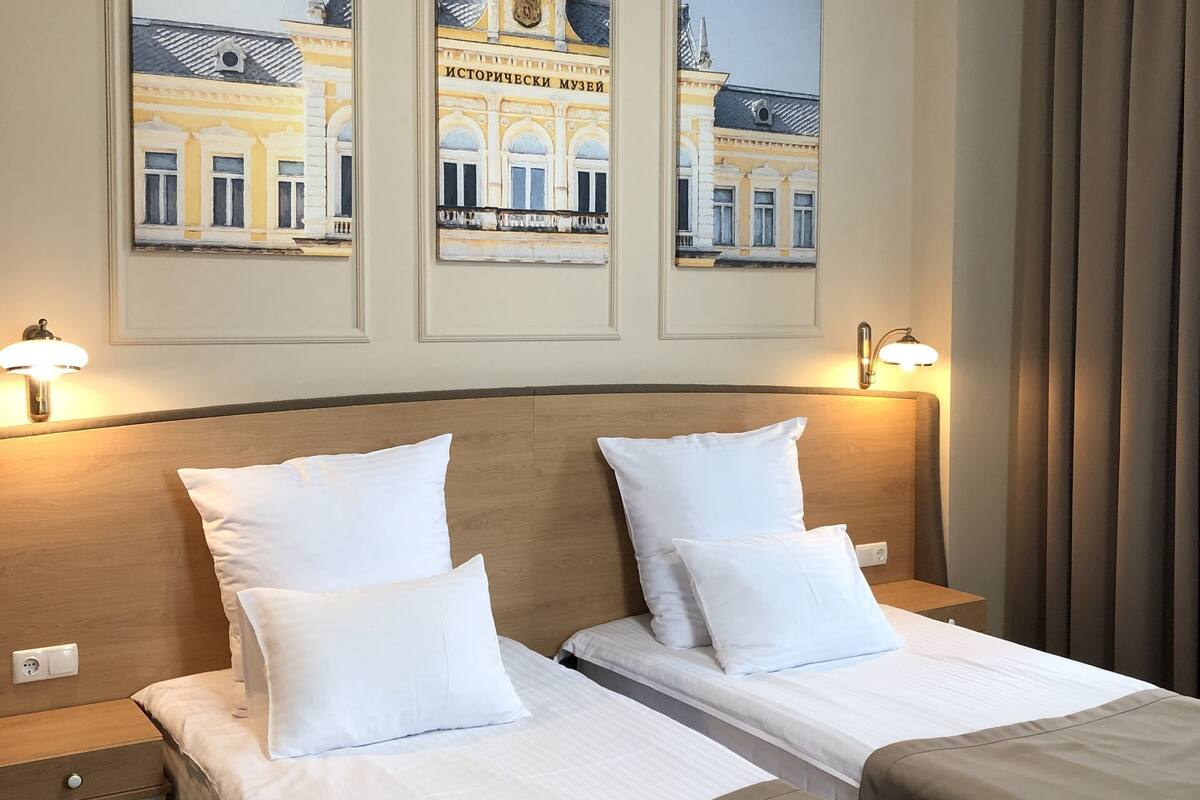 A hotel room with two beds, a headboard, bedside tables, lamps, and three framed pictures on the wall.