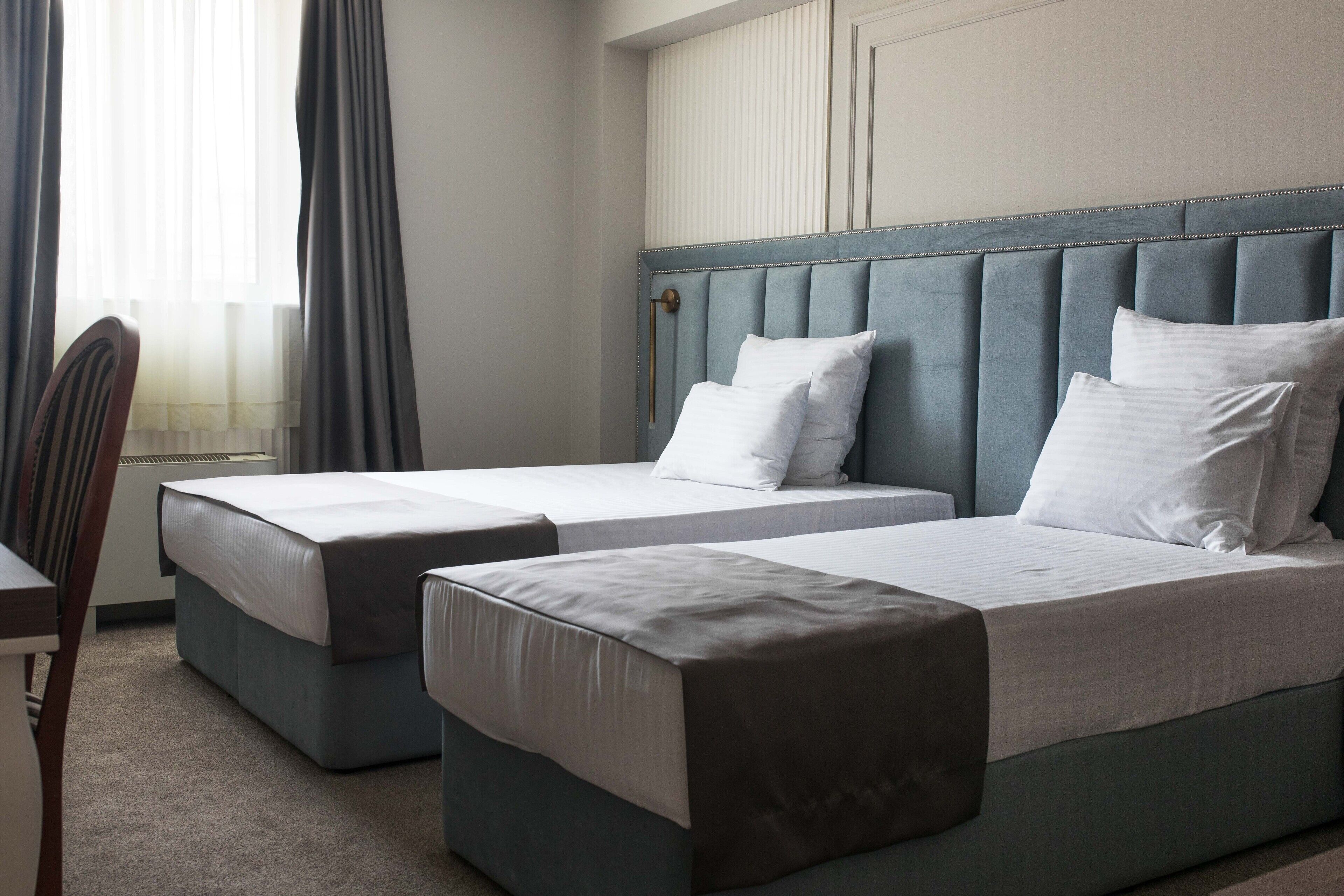 A hotel room with two single beds, a chair, and a window with curtains.