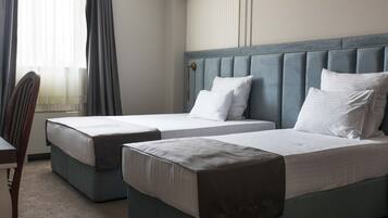 A hotel room with two single beds, a chair, and a window with curtains.