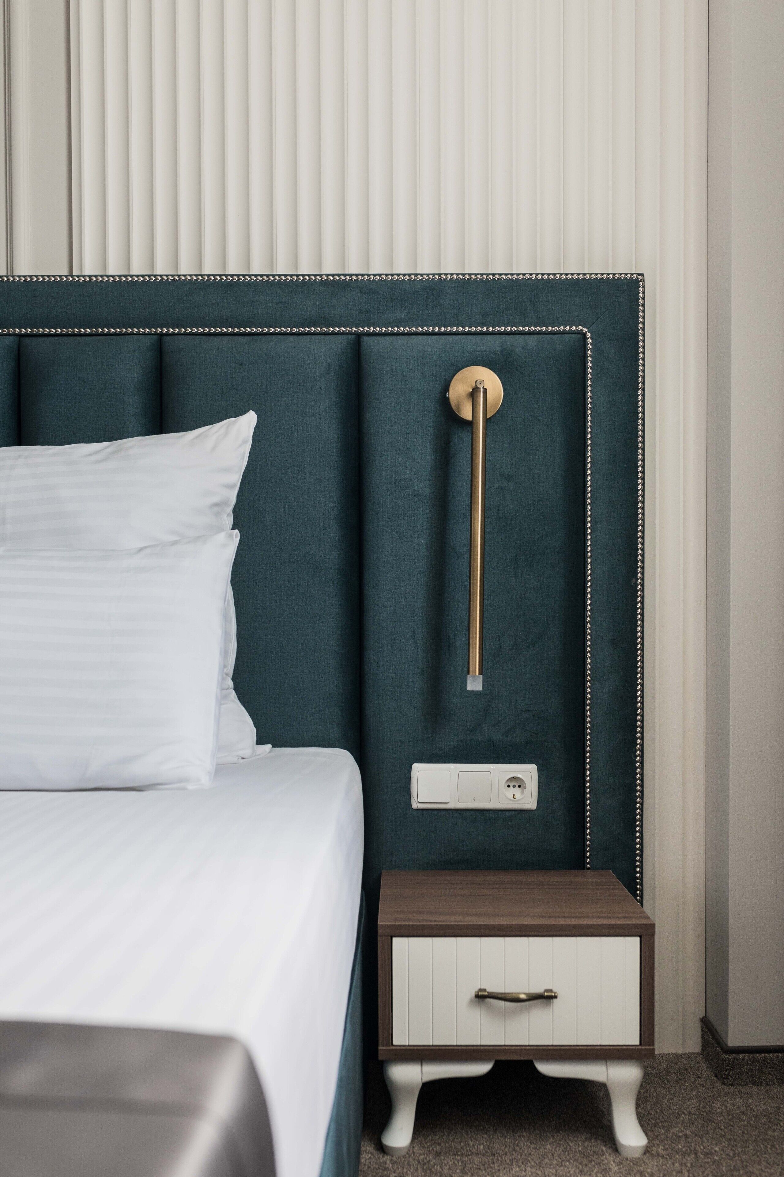 A neatly made bed with white linens, a teal upholstered headboard, and a bedside table with a drawer.