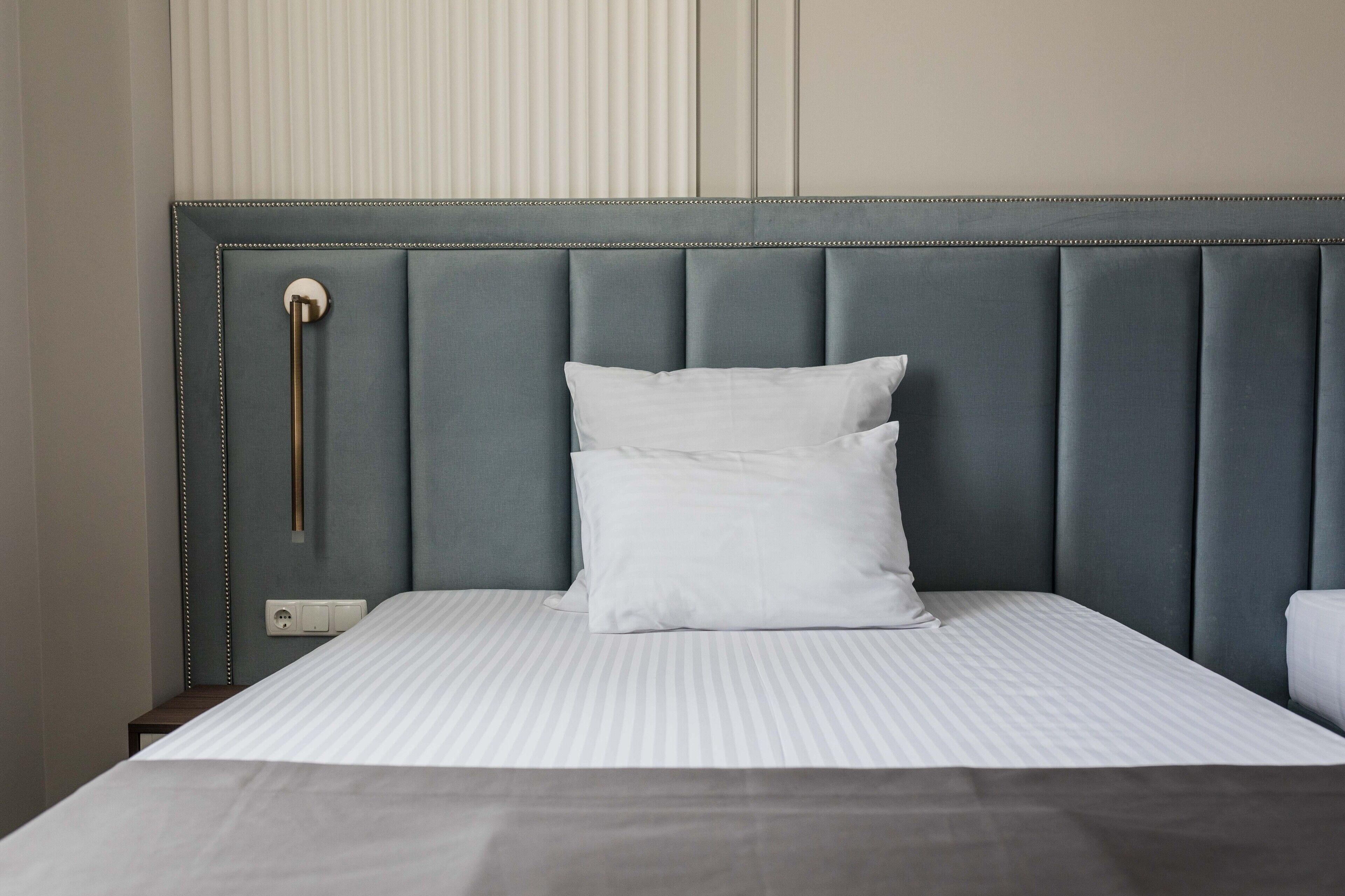 A neatly made bed with a grey upholstered headboard, white pillows, and a striped bedspread.