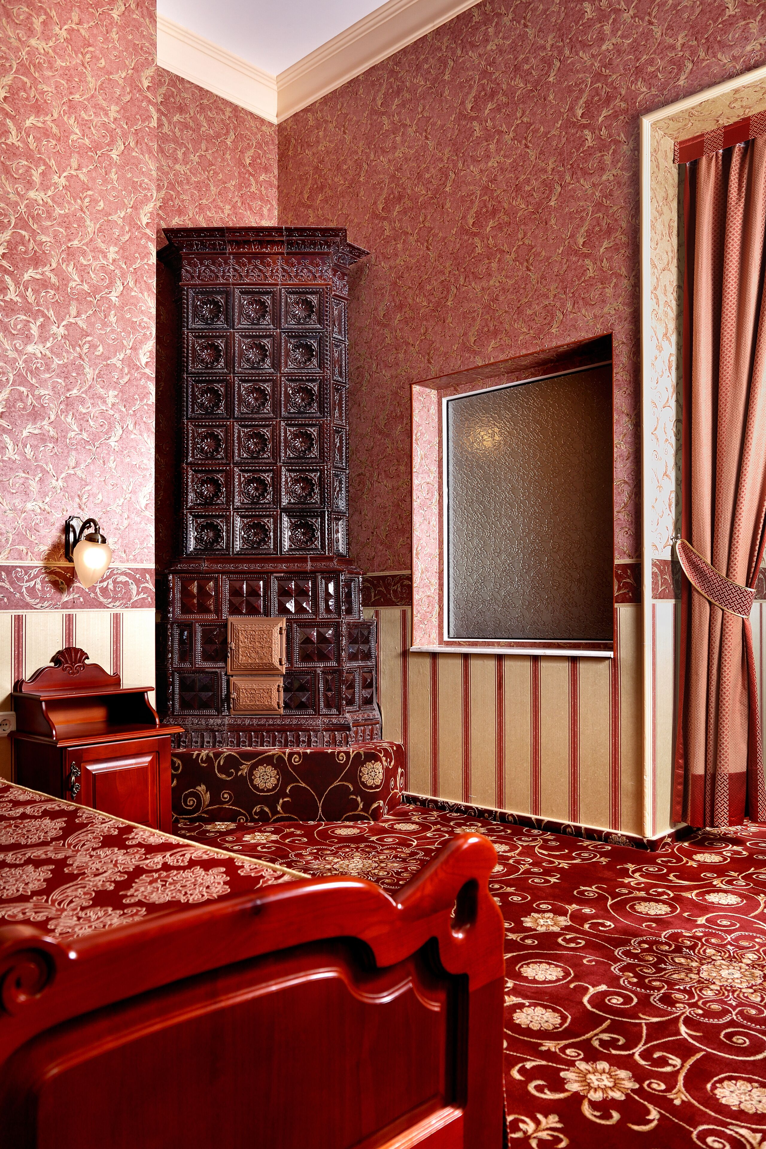 A room with a large bed, a wooden cabinet, a wall-mounted TV, and patterned wallpaper.