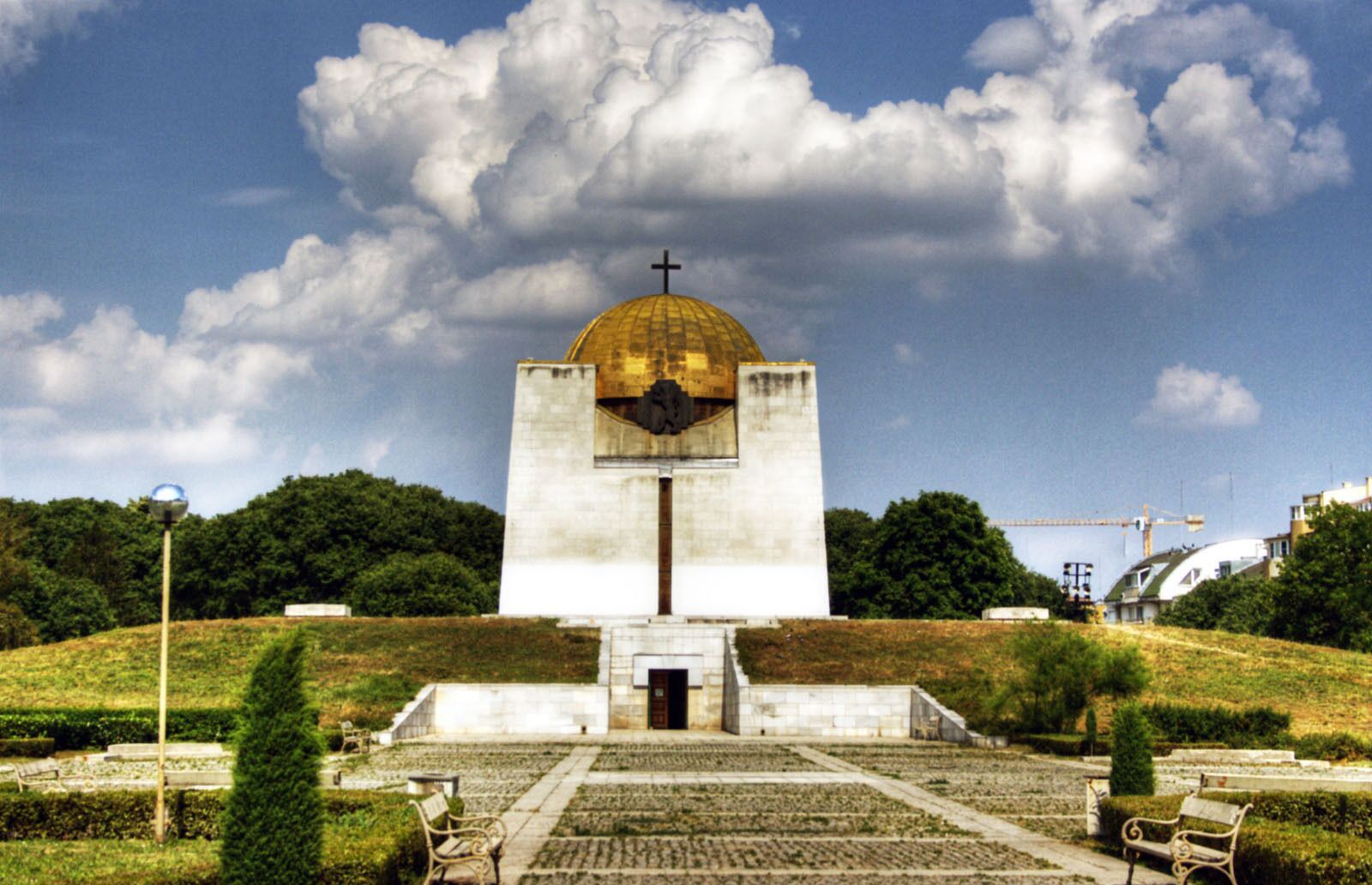 A church with a golden dome and a cross on top, surrounded by a landscaped area with benches.