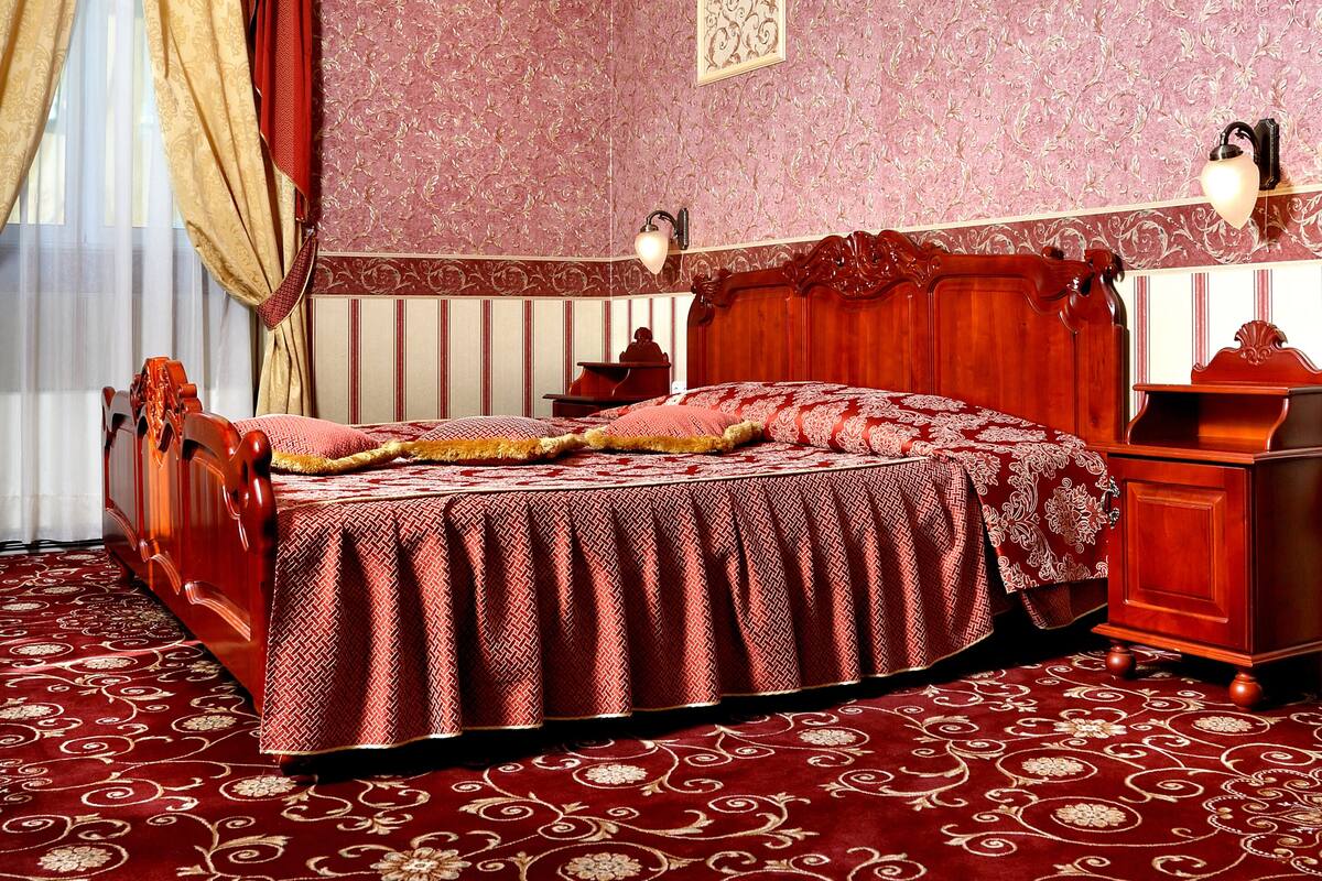 A room with a large bed, a wooden nightstand, a desk, and a chandelier.