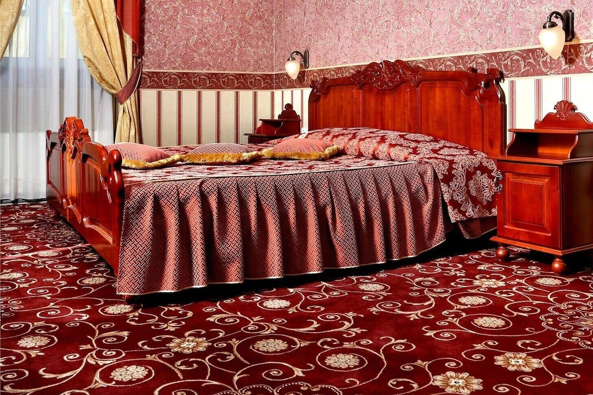 A bedroom with a large bed, a wooden headboard, a red carpet, and a chandelier.