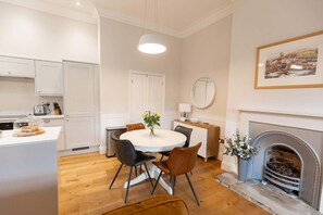 Une cuisine moderne avec des meubles blancs, un coin repas comprenant une table ronde et des chaises, une cheminée et un tableau encadré au mur.