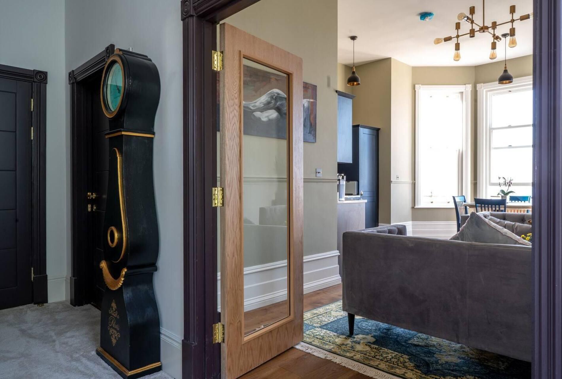 Quarto com uma grande porta de madeira, um piano preto, um sofá cinza e um candelabro.