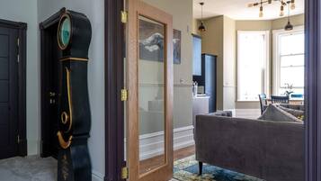 Quarto com uma grande porta de madeira, um piano preto, um sofá cinza e um candelabro.